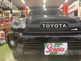 【当社のハイラックスサーフは新品フロントグリルを装着しております】トヨタのインパクトあるTOYOTAエンブレムを施したタコマ型グリル。迫力あるフロントフェイスとなり、ひときわ目立った存在感を放つ。