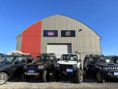 CarBase.Jimnyは、グレーとレッドのツートンカラーの大きい倉庫の中に事務所があります。